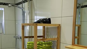 A bathroom with a wooden shelf holding green towels, a white sink, and a mirror above it.