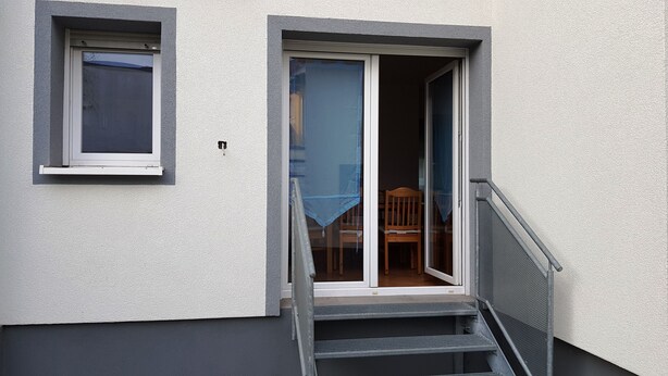 Un immeuble résidentiel avec une petite fenêtre et une porte donnant sur une pièce où se trouvent une chaise et une table.