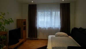 Une chambre avec un lit, une télévision, une armoire en bois et une fenêtre avec des rideaux.