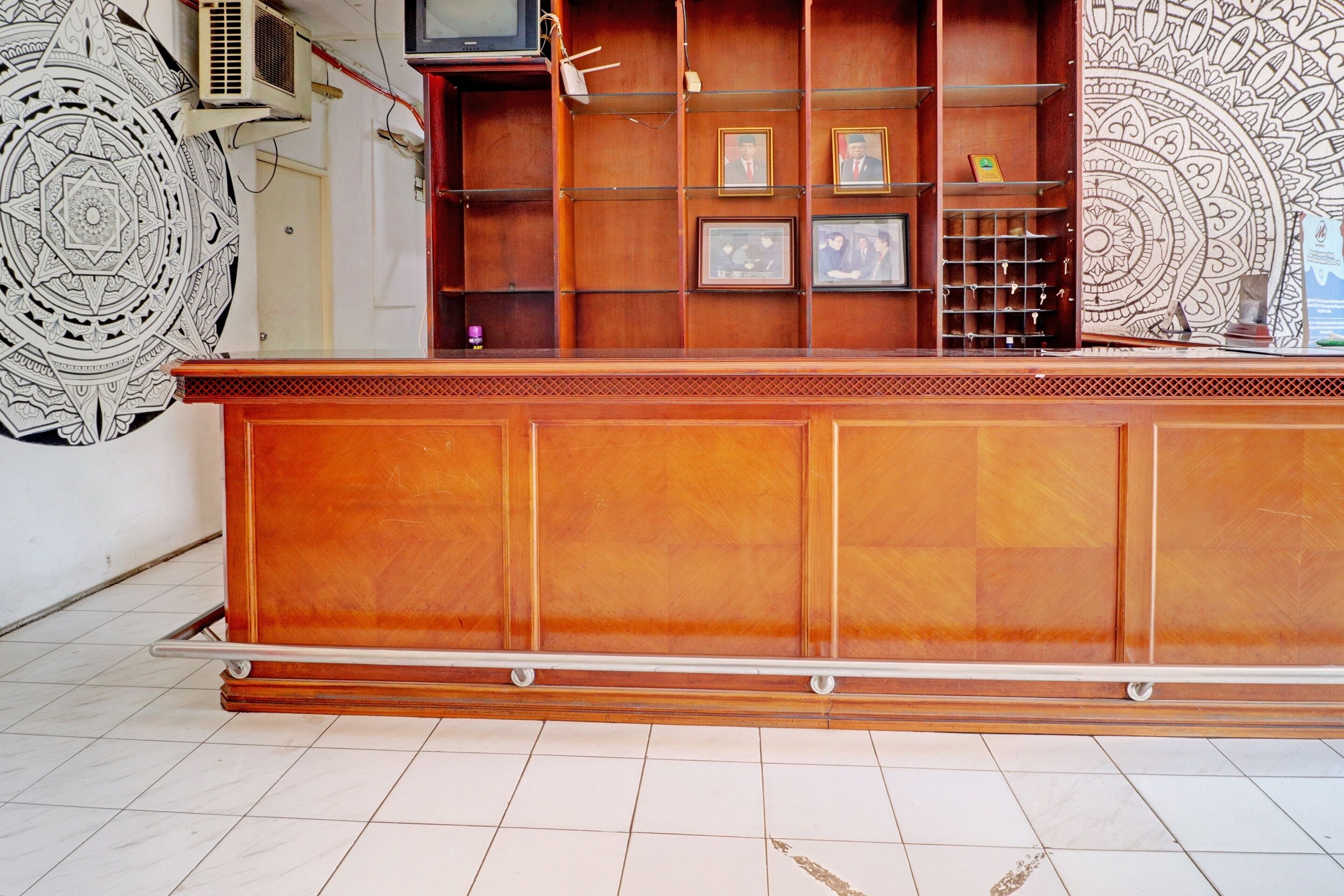 A reception desk with a wooden finish, a tiled floor, and a wall with a large circular design.
