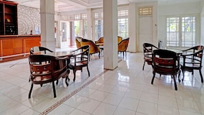 A spacious lobby with a high ceiling, tiled floor, and several wooden chairs and tables arranged for seating. - OYO 2452 Hotel Metro (Bandung)