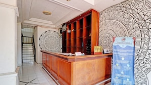 A reception desk with a patterned wall and a blue informational sign. - OYO 2452 Hotel Metro (Bandung)