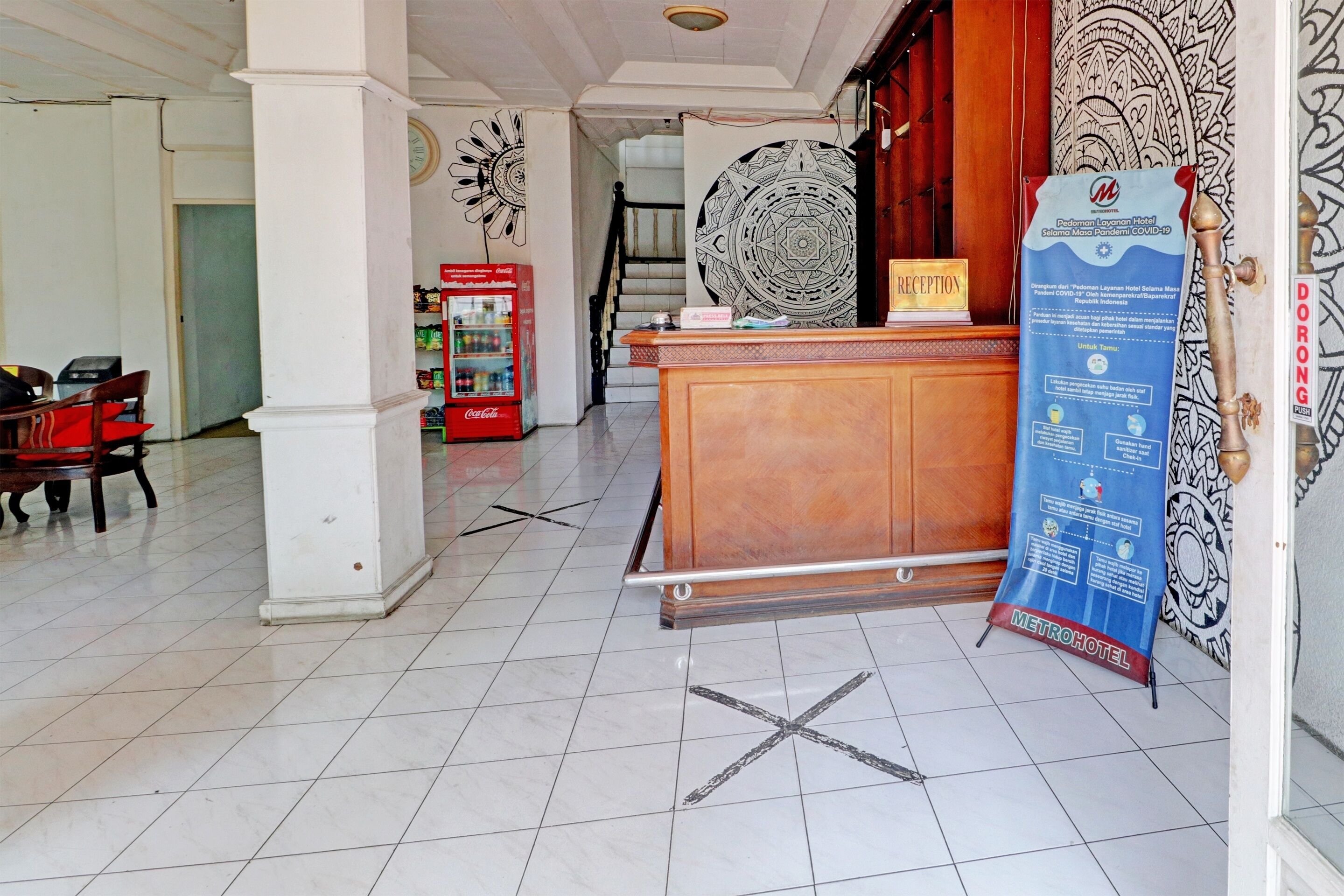 A hotel reception area with a reception desk, a Coca-Cola refrigerator, a staircase, and a reception sign.