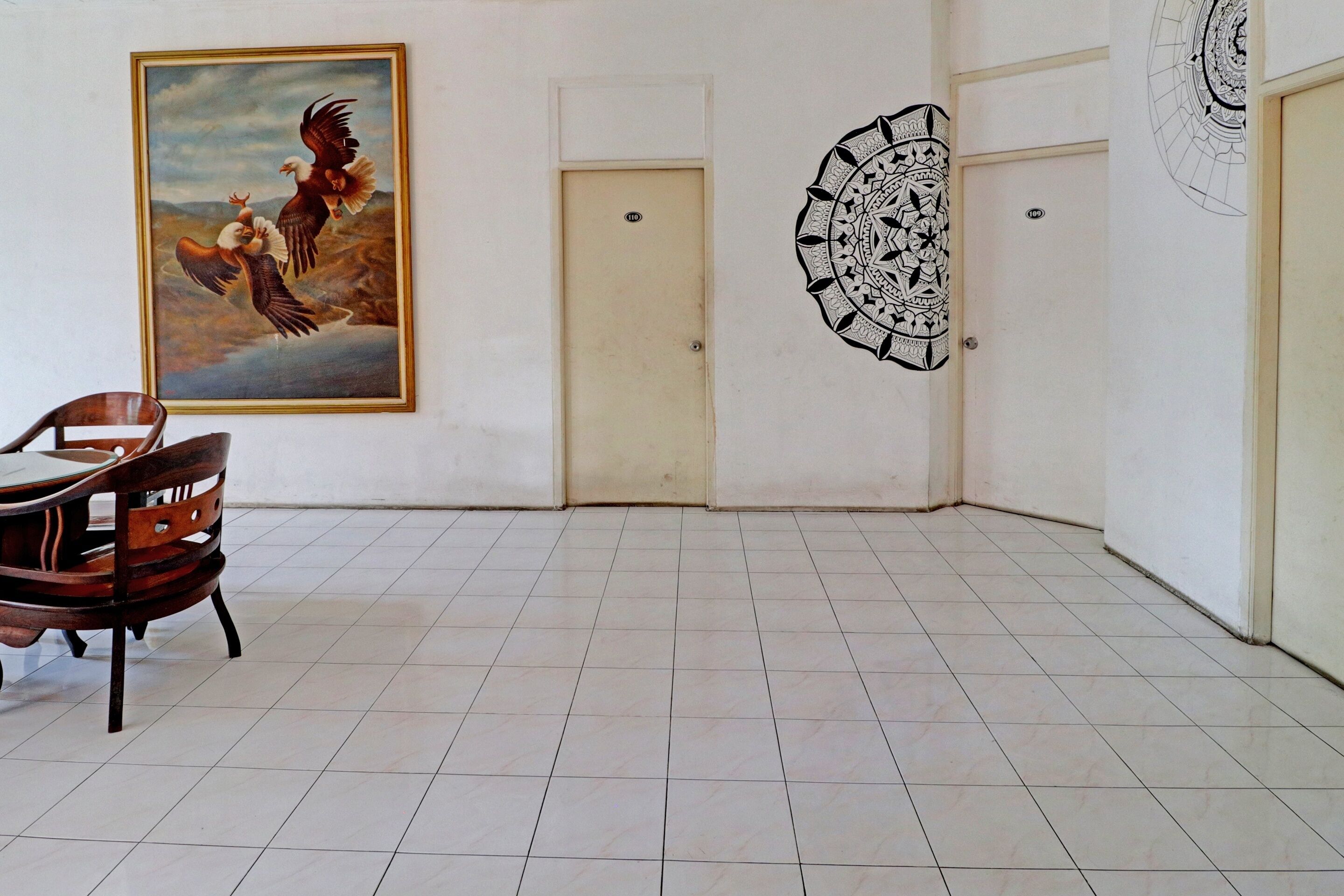 Une pièce avec un sol carrelé, une chaise en bois, une porte et un mur orné d’un tableau et d’un motif circulaire.