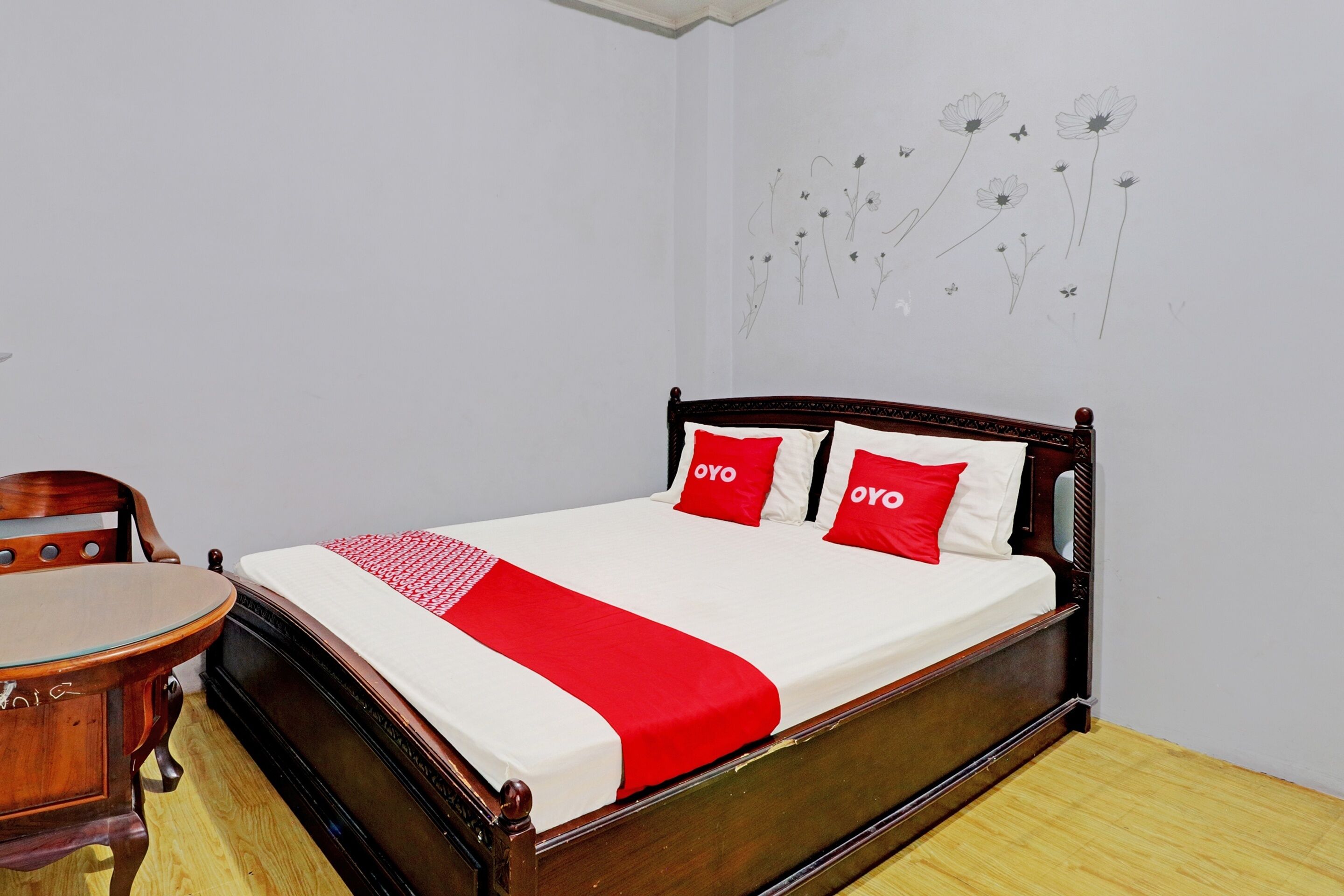 A neatly made bed with a red and white bedspread, two red pillows with the word "OYO" on them, and a wooden headboard.
