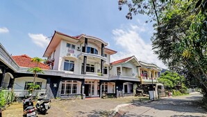 A multi-story building with a red-tiled roof, a sign indicating a business, and a paved driveway with parked motorcycles. - OYO 2452 Hotel Metro (Bandung)