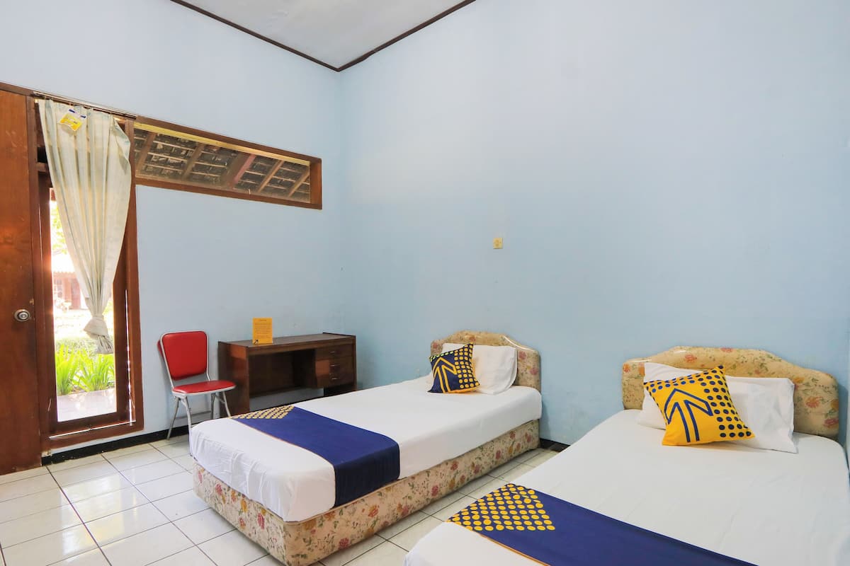 A room with two beds, a chair, a desk, and a door leading outside.