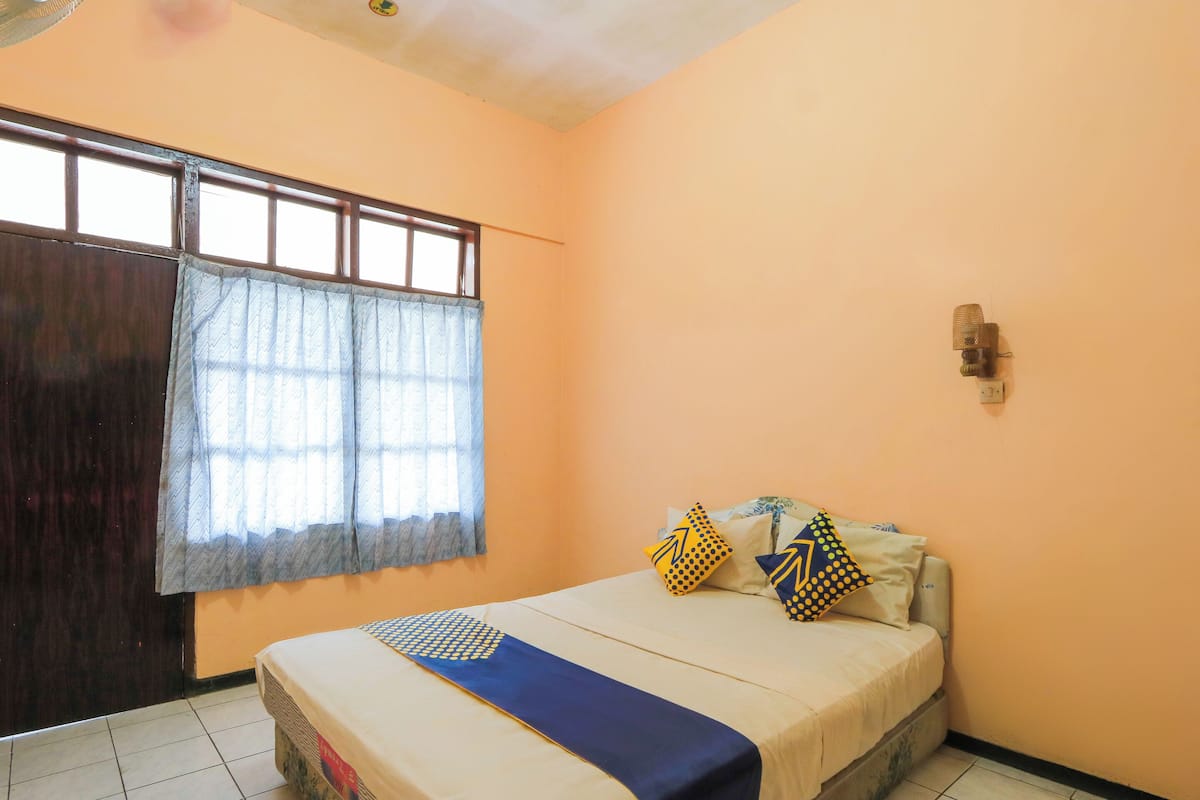 A bedroom with a bed, a window with curtains, a wall-mounted light, and a wooden door.