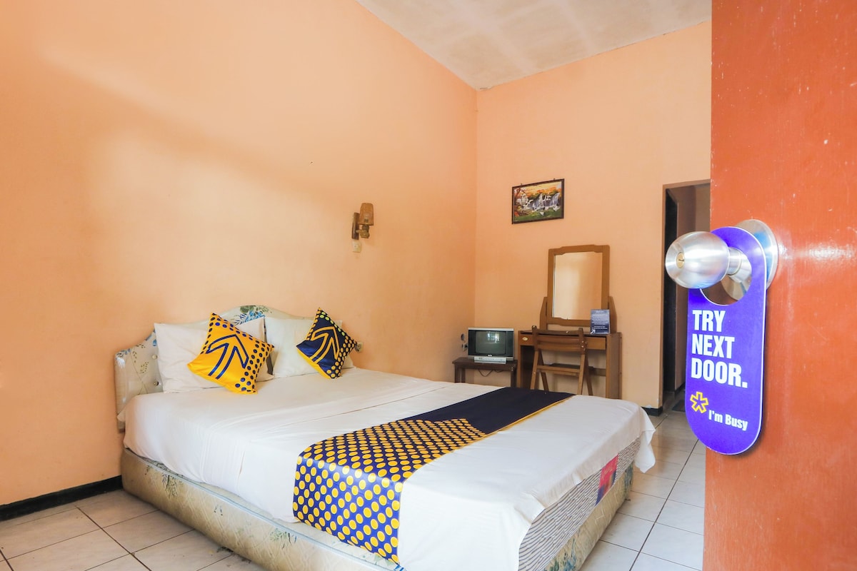 A bedroom with a bed, a television, a desk, and a door with a sign.