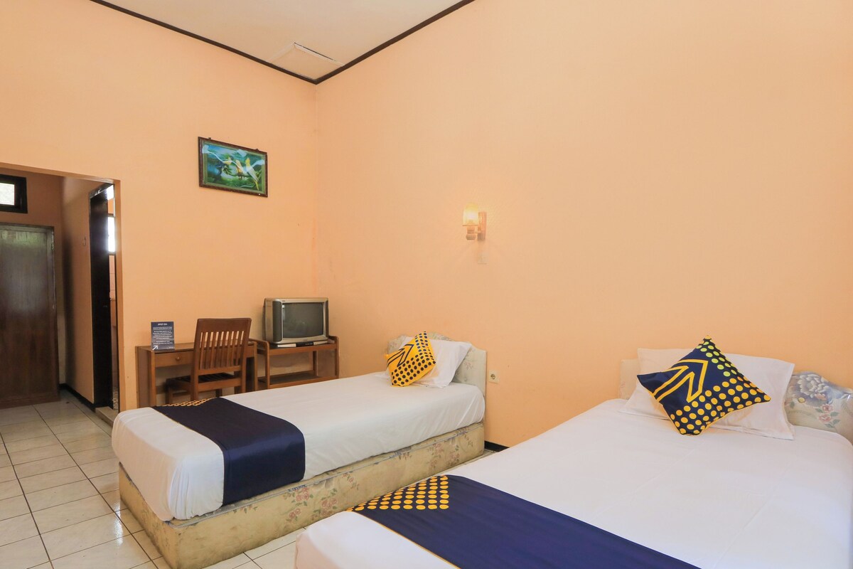 A hotel room with two beds, a desk with a television, and a door leading to another room.