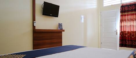 Une chambre d’hôtel avec un lit, une tête de lit en bois, un téléviseur à écran plat fixé au mur, une porte et une fenêtre avec des rideaux.