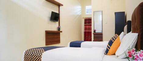 A hotel room with two beds, a TV mounted on the wall, a small table with a vase of flowers, and an air conditioning unit.