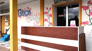 Ein Empfangsschalter im Holz- und Weißdesign, eine Wand mit farbenfrohen Graffiti und ein Schild für Wisma&Cafe.