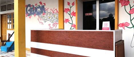 Una recepción con diseño de madera y blanco, una pared con grafitis coloridos y un cartel de Wisma&Cafe.
