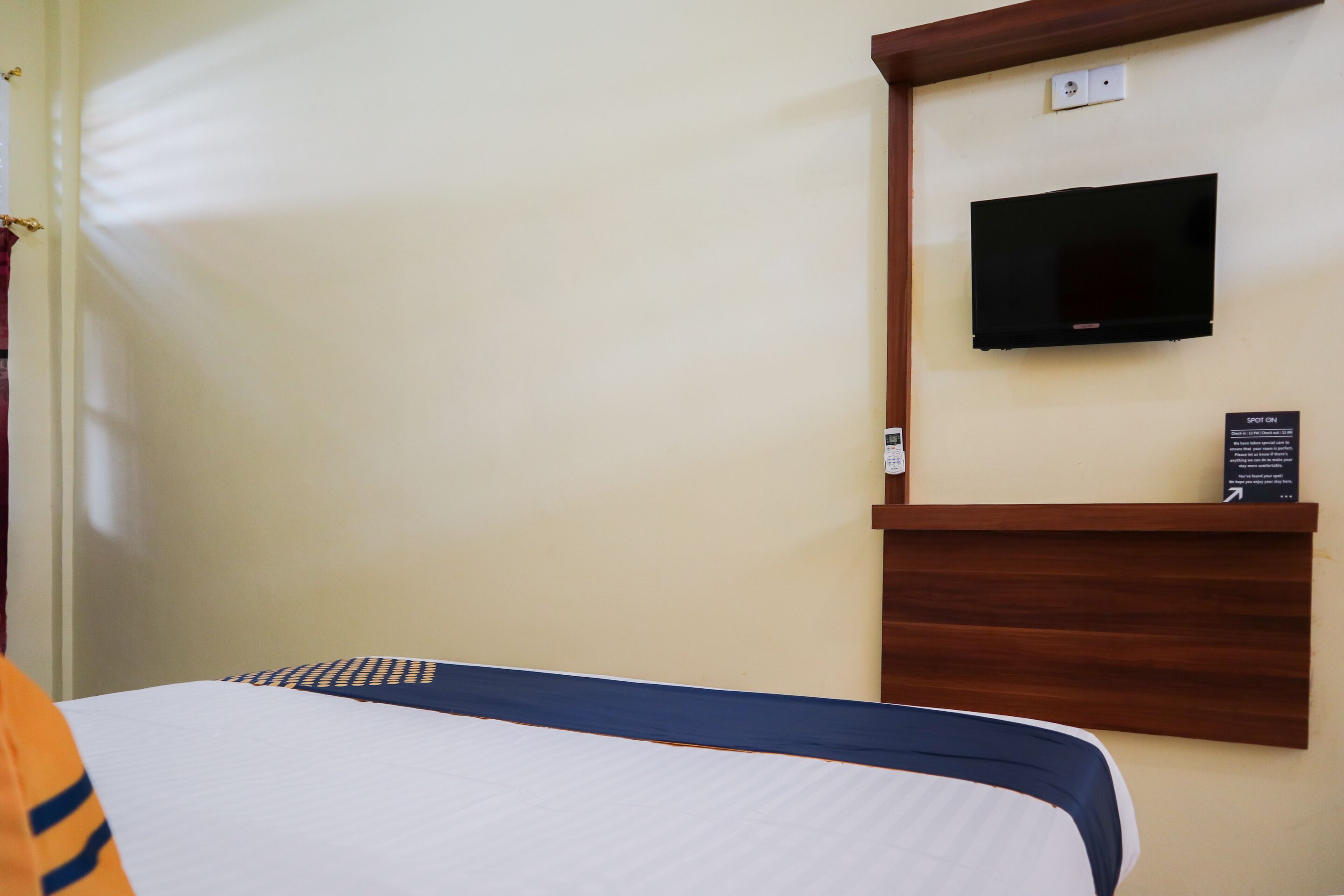 Een hotelkamer met een bed, een wandtelevisie en een houten plank met een bordje.