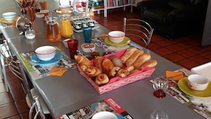 Ein langer Esstisch mit verschiedenen Frühstücksangeboten, ein Bücherregal im Hintergrund und ein schwarzes Ledersofa.