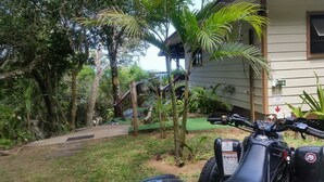 A garden area with a pathway leading to a building, surrounded by trees and a parked motorcycle. - Campismo Ninho 11 (Ponta d'Ouro)