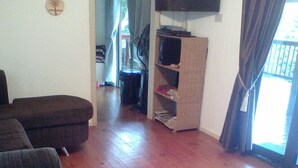A living room with a sofa, a television mounted on the wall, and a wooden floor. - Campismo Ninho 11 (Ponta d'Ouro)