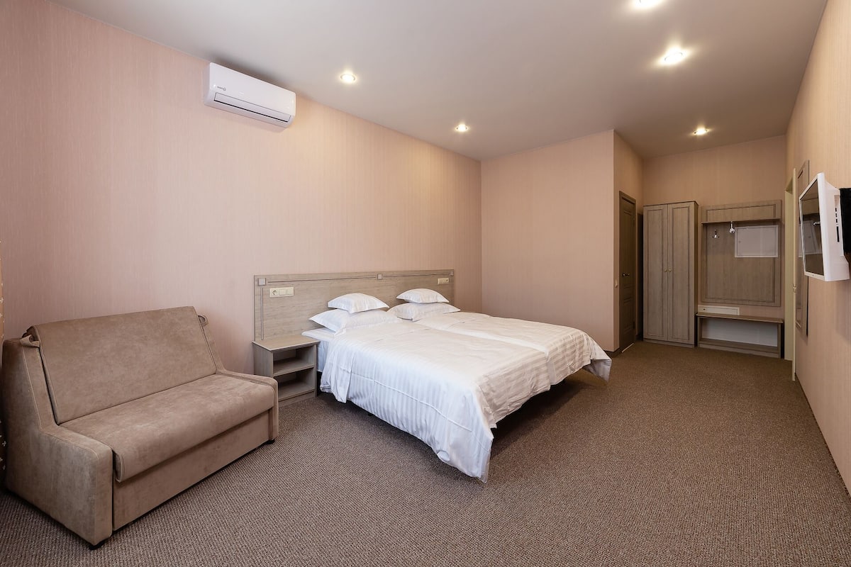 Et hotelværelse med en seng, en stol, et skab og en aircondition.
