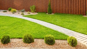 Un jardín bien cuidado con cerca de madera, un sendero serpenteante y arbustos podados.