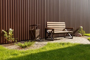 A bench and a trash bin against a corrugated metal wall.