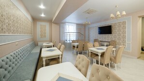 Un comedor de hotel con un largo banco, varias mesas con sillas, una escalera y un televisor montado en la pared.