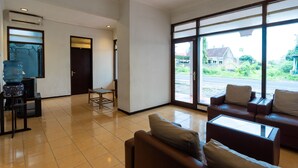 A spacious room with a large window, a sofa, a table, and a water dispenser. - OYO 2454 Wanawiyata Homestay  (Depok)