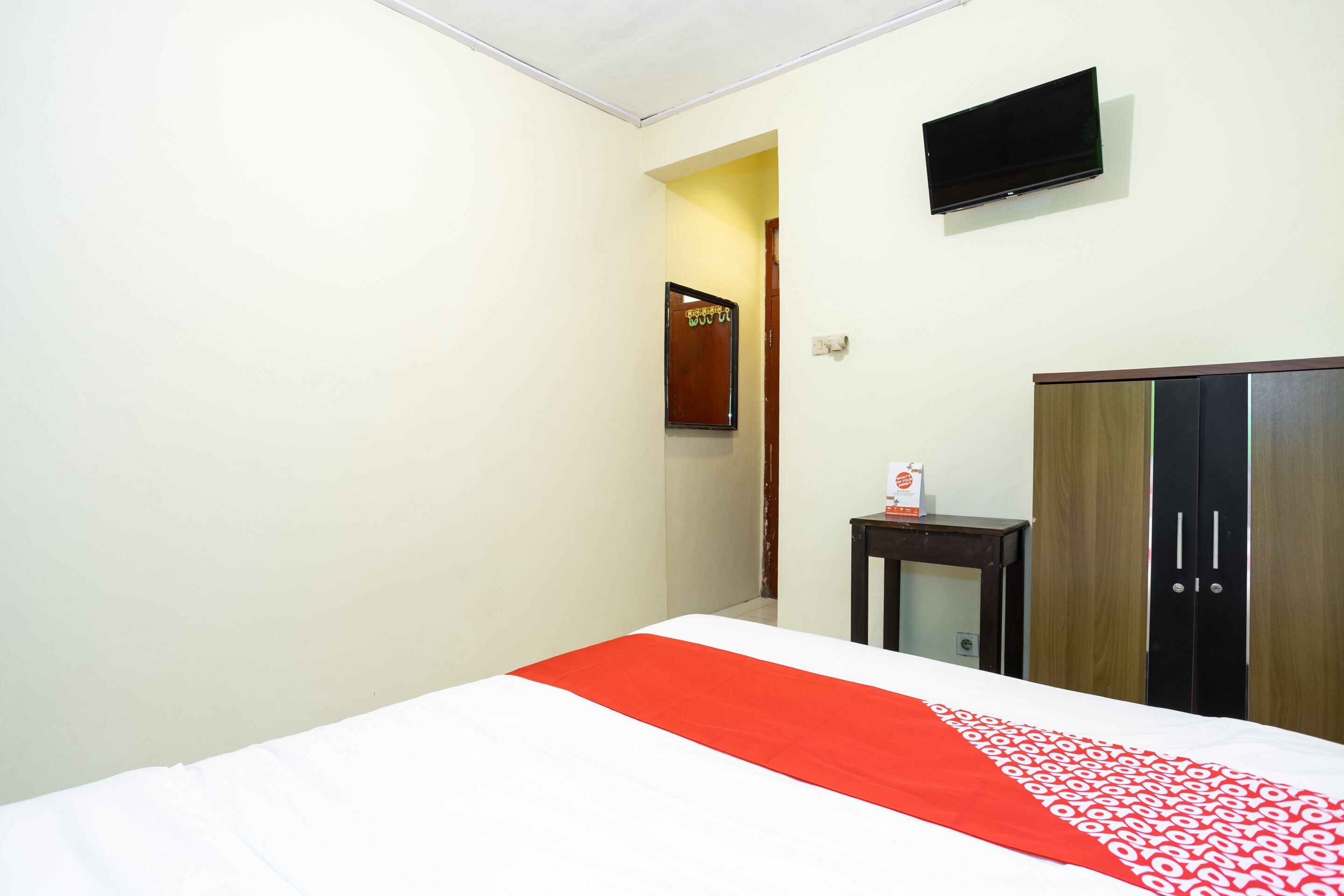 A hotel room with a bed, a television mounted on the wall, and a wardrobe.