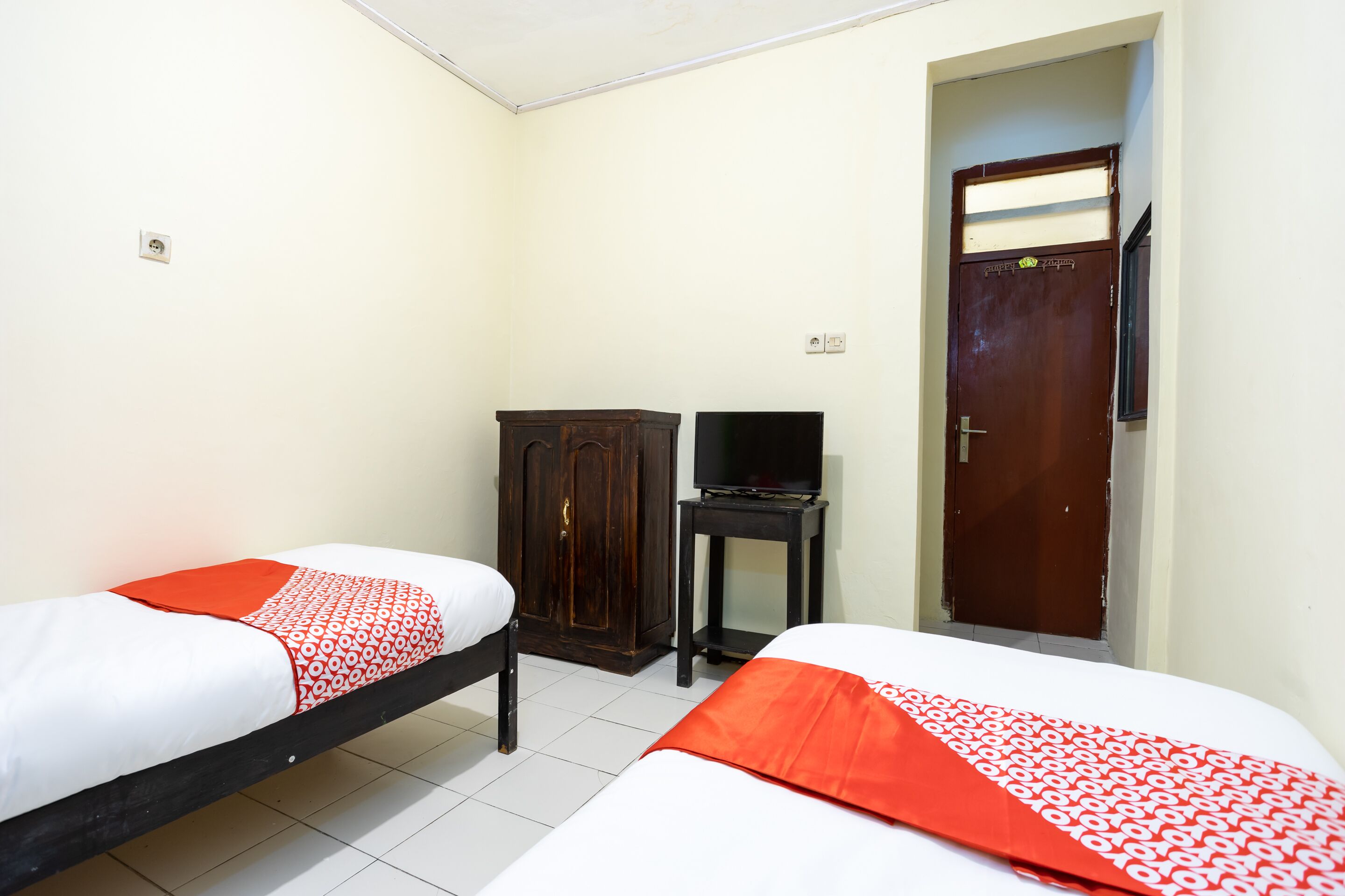 A room with two beds, a wardrobe, a television, and a door.