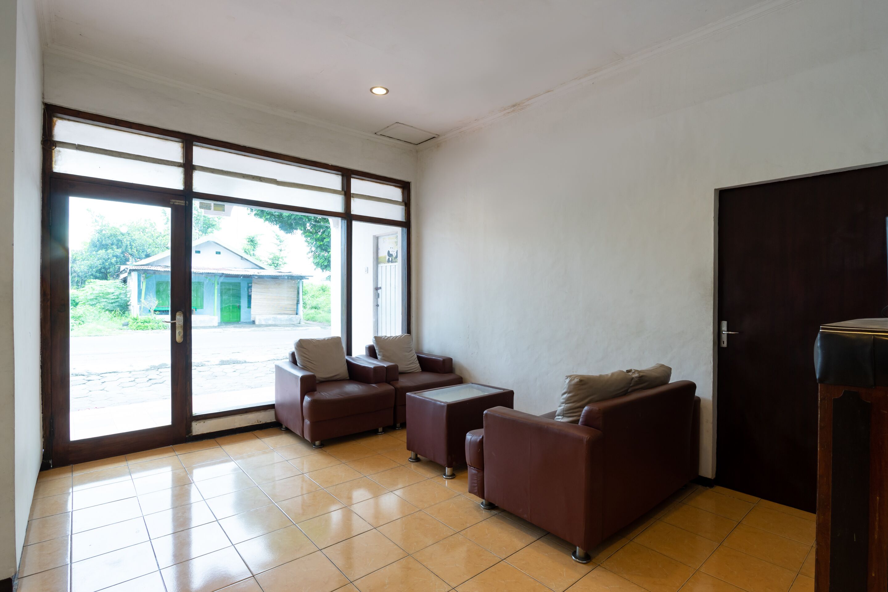 A spacious room with a large sliding glass door leading to an outdoor area, furnished with brown leather sofas and a small table.