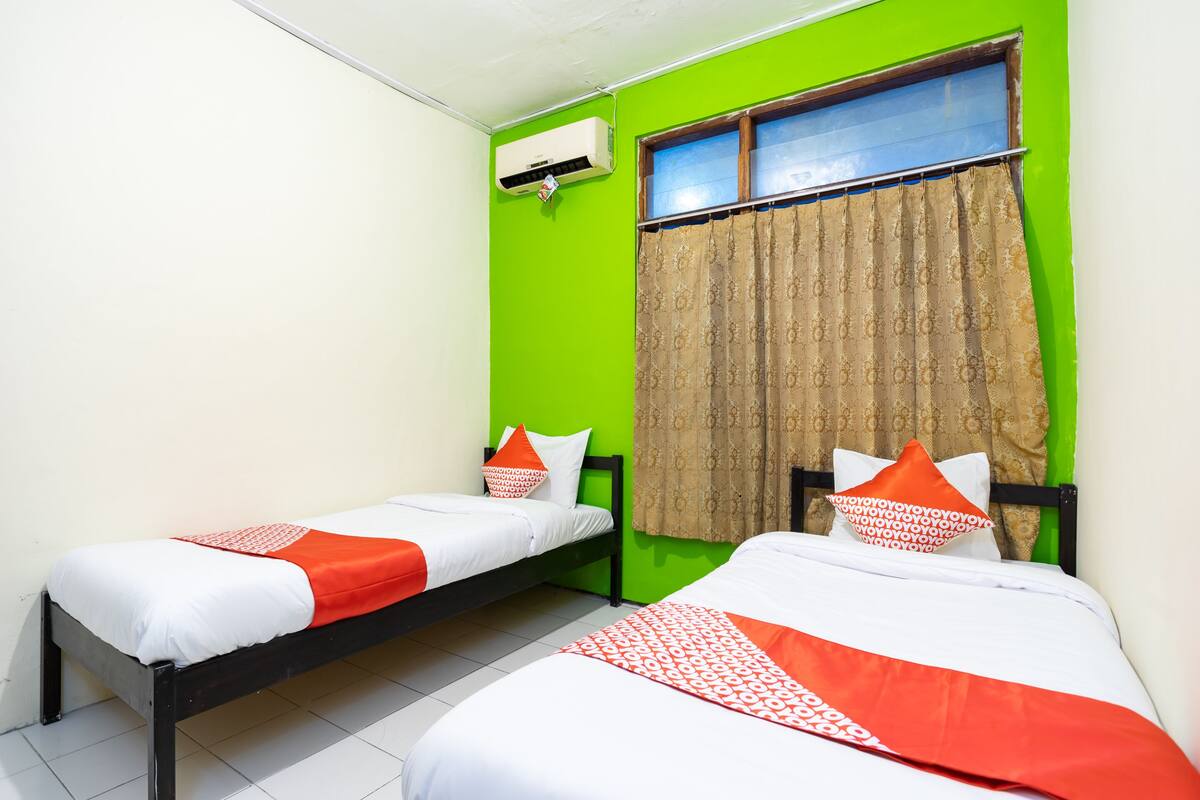 Una habitación con dos camas, una ventana con cortinas, un aire acondicionado y una pared verde.