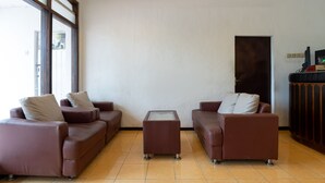 A living room with two brown leather sofas, a glass coffee table, and a dark wooden cabinet. - OYO 2454 Wanawiyata Homestay  (Depok)