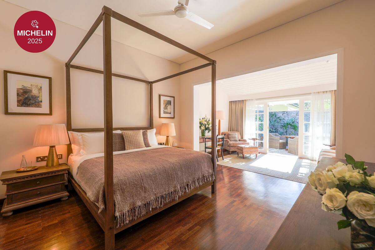 A four-poster bed with a wooden frame, a nightstand with a lamp, and a vase of white flowers.