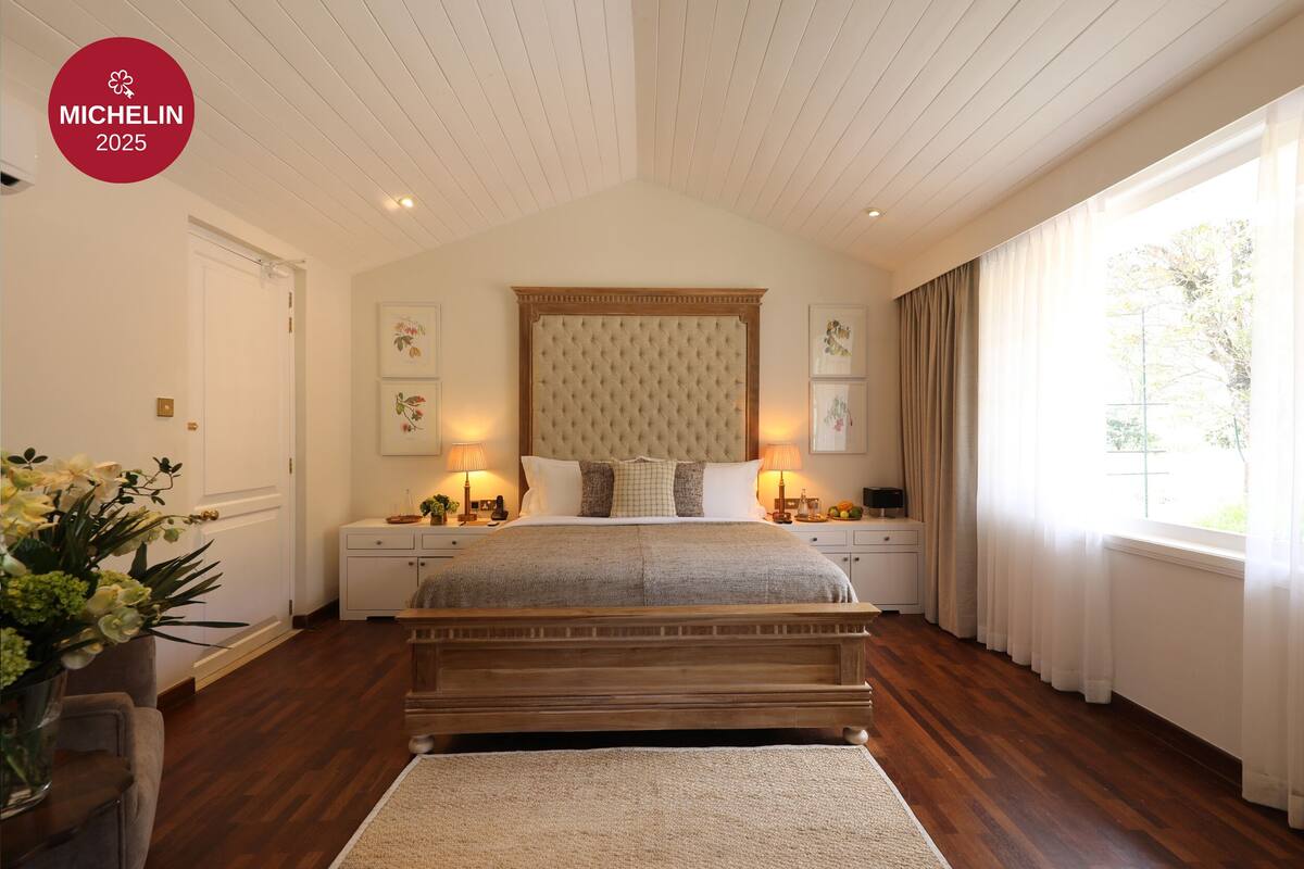 A bedroom with a large bed, wooden headboard, bedside lamps, and a window with curtains.