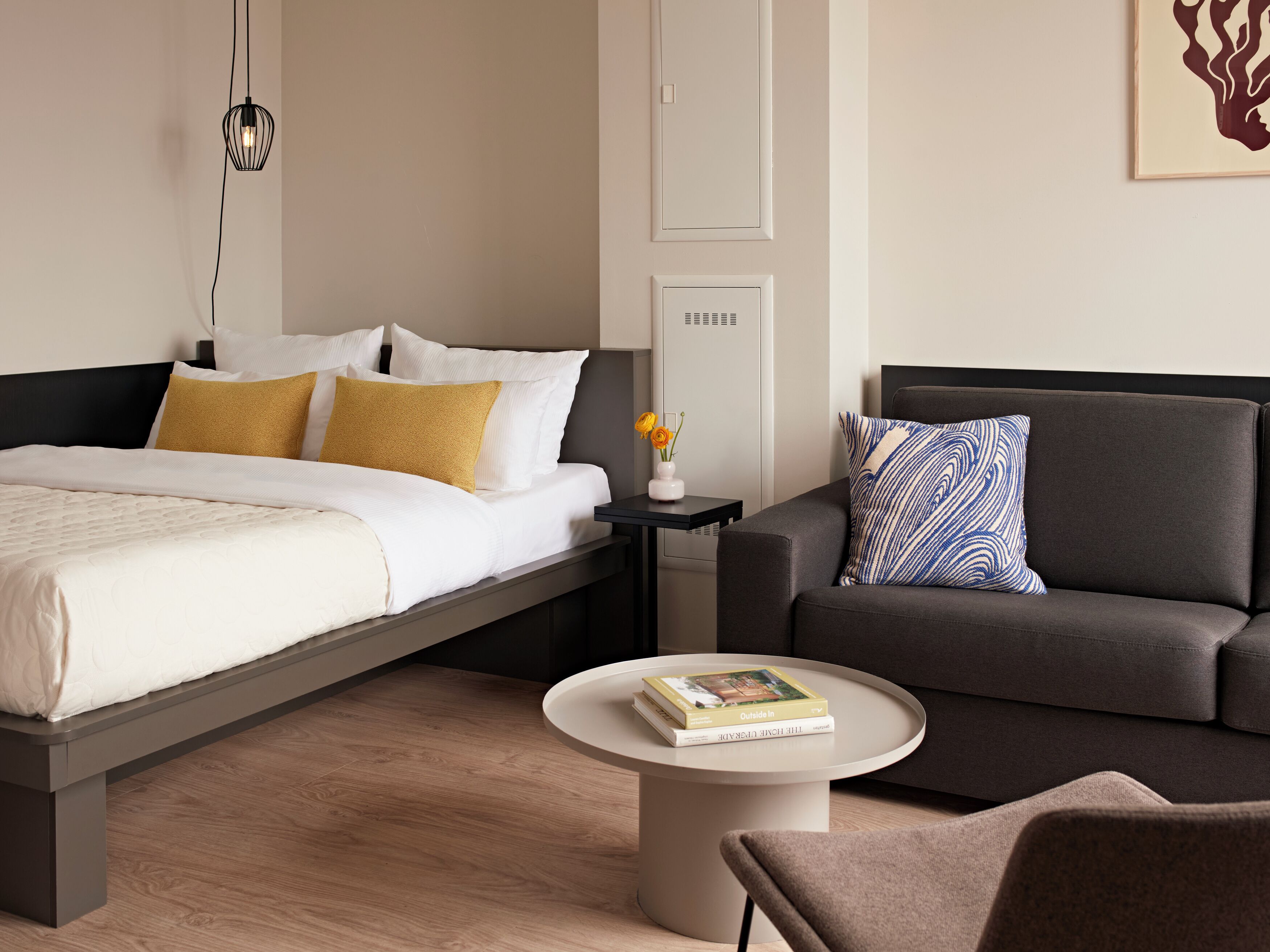 A modern hotel room with a bed, a sofa, a coffee table, and a nightstand.