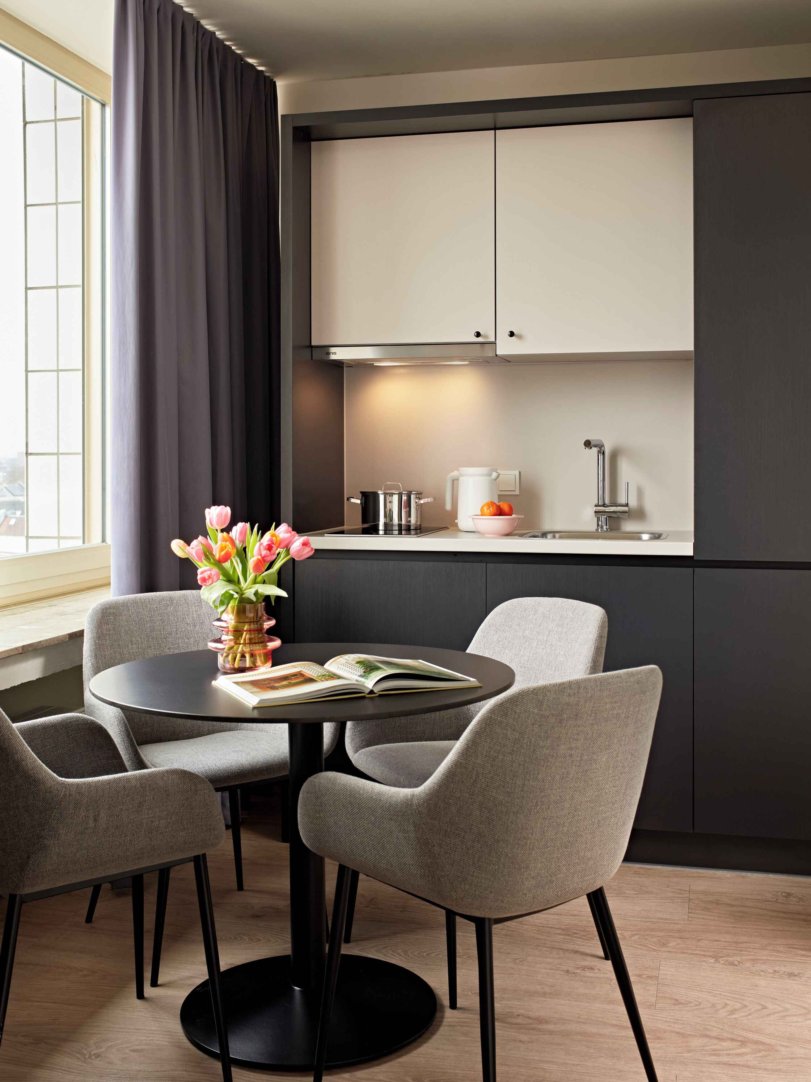 Una cocina moderna con armarios oscuros, una mesa redonda con sillas, un jarrón de flores y un libro.