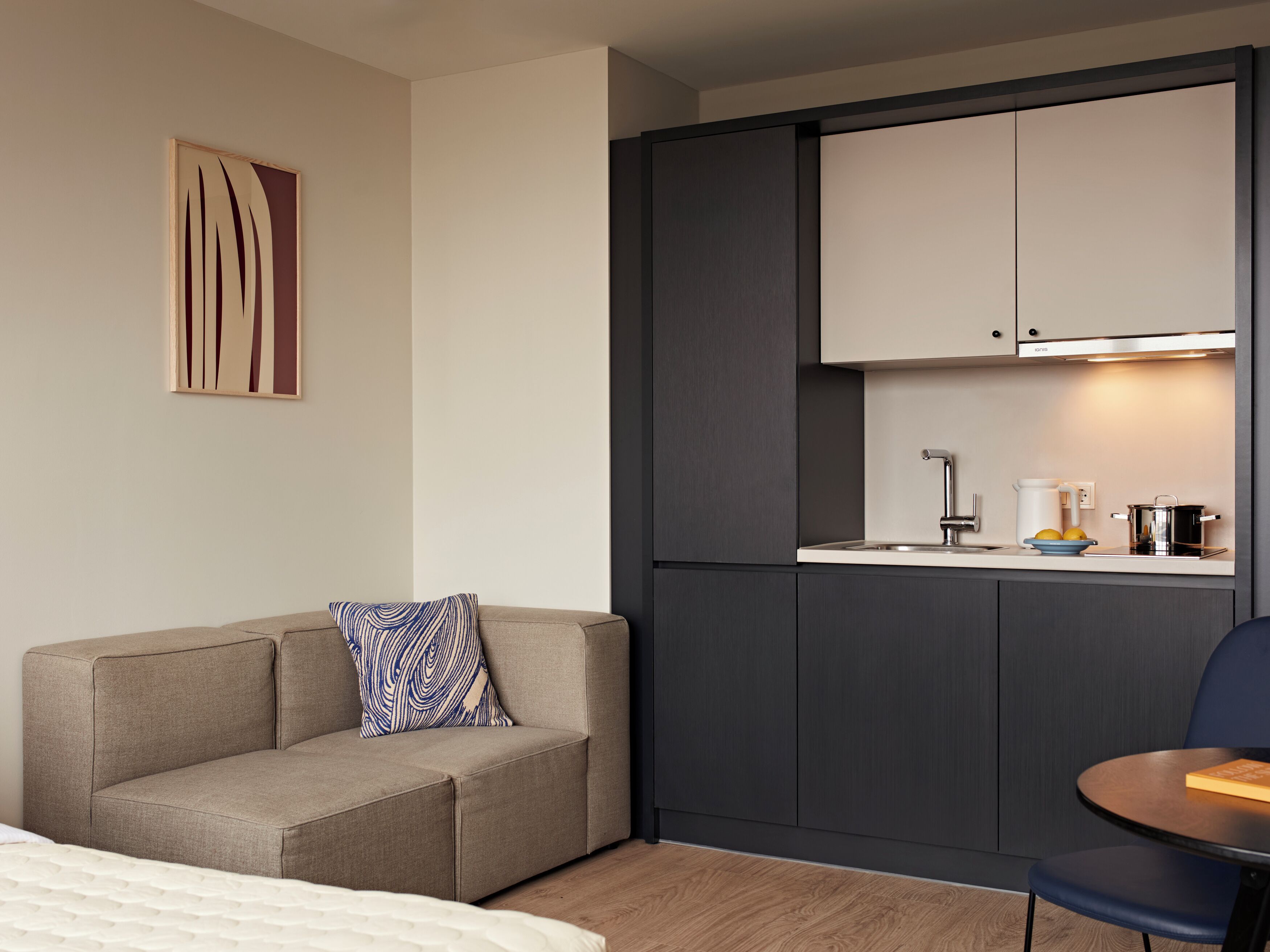 Une chambre d’hôtel moderne équipée d’un canapé, d’une petite table, d’une kitchenette et d’un lit.