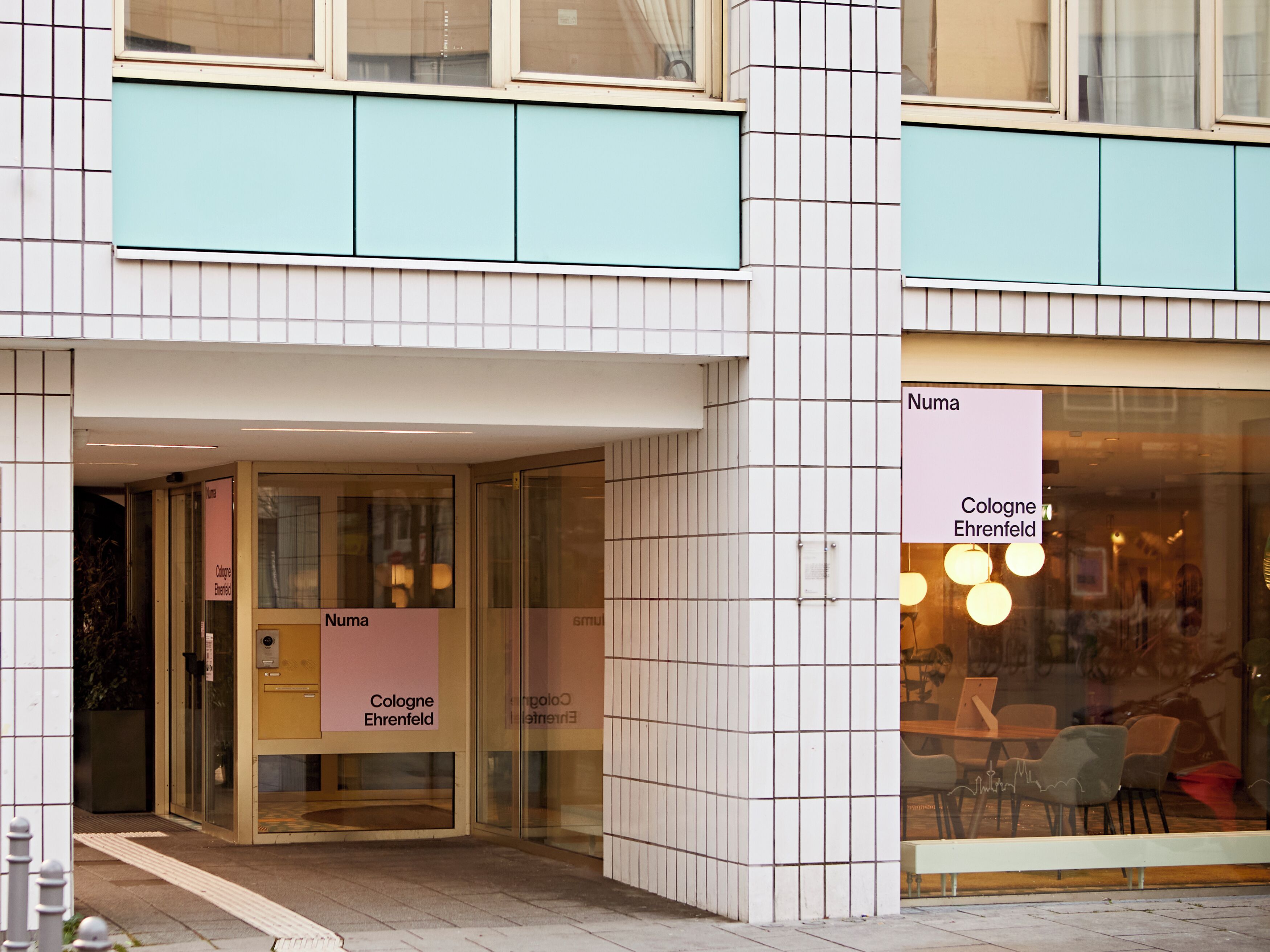 Un edificio con fachada de tejas, puertas de vidrio y señalización que indica 'Cologne Ehrenfeld'.