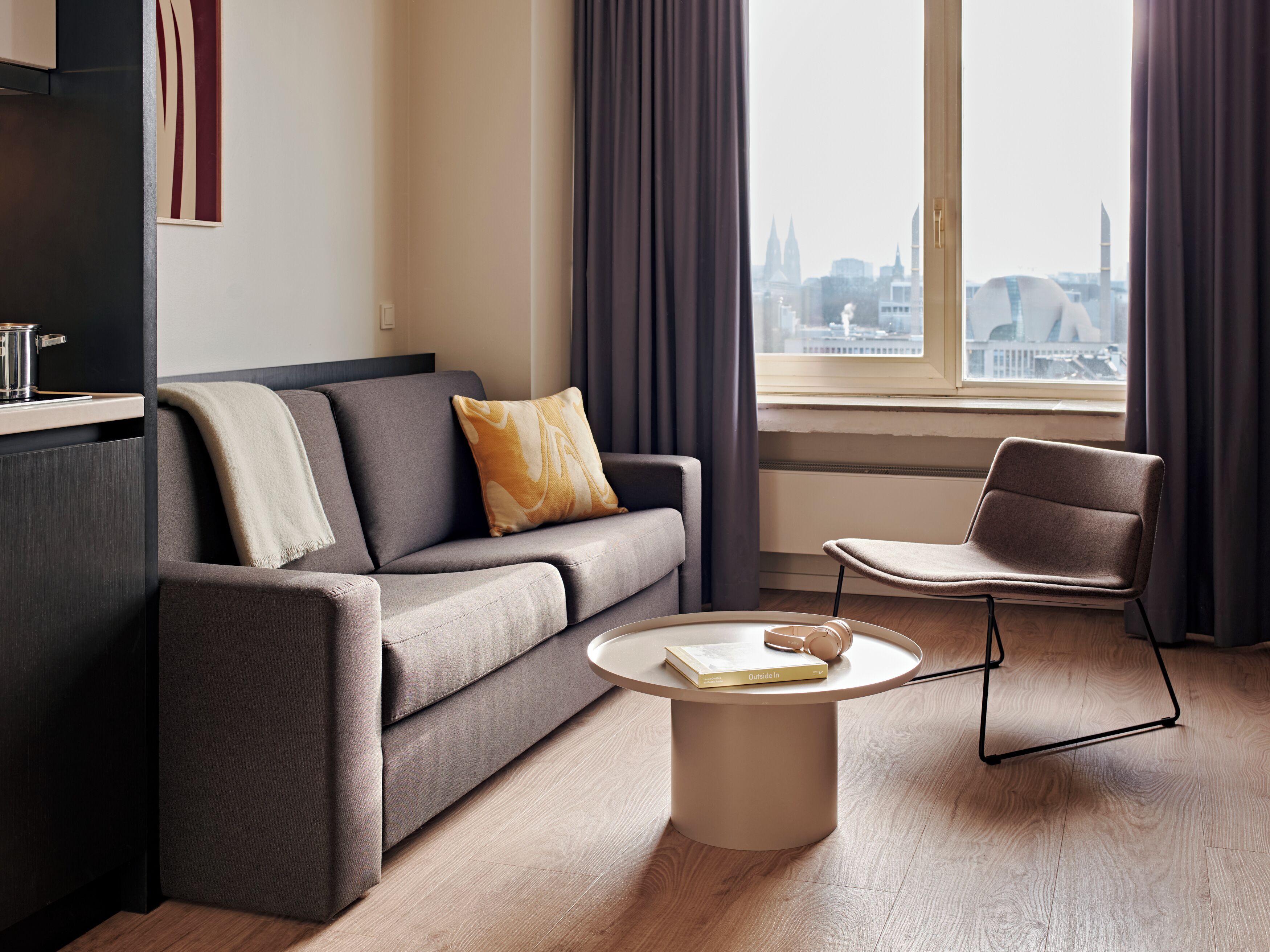 Ein modernes Wohnzimmer mit einer Couch, einem Sessel, einem Couchtisch und Blick auf eine Stadtlandschaft durch ein Fenster.