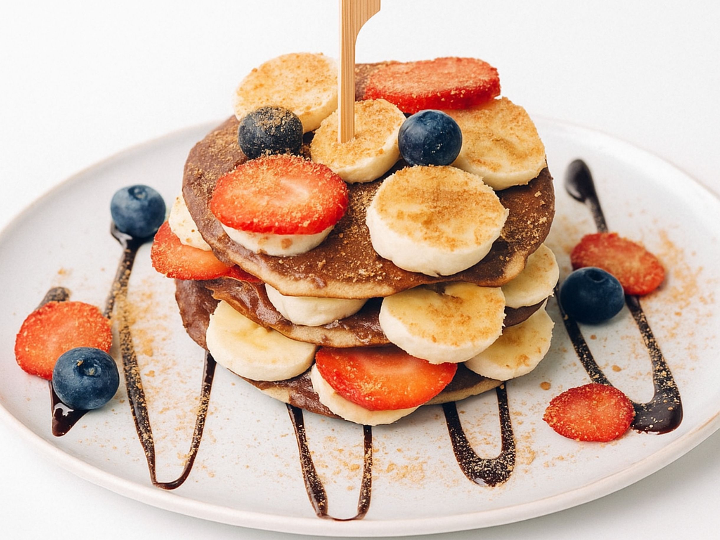 A stack of pancakes with strawberries and blueberries on a white plate.