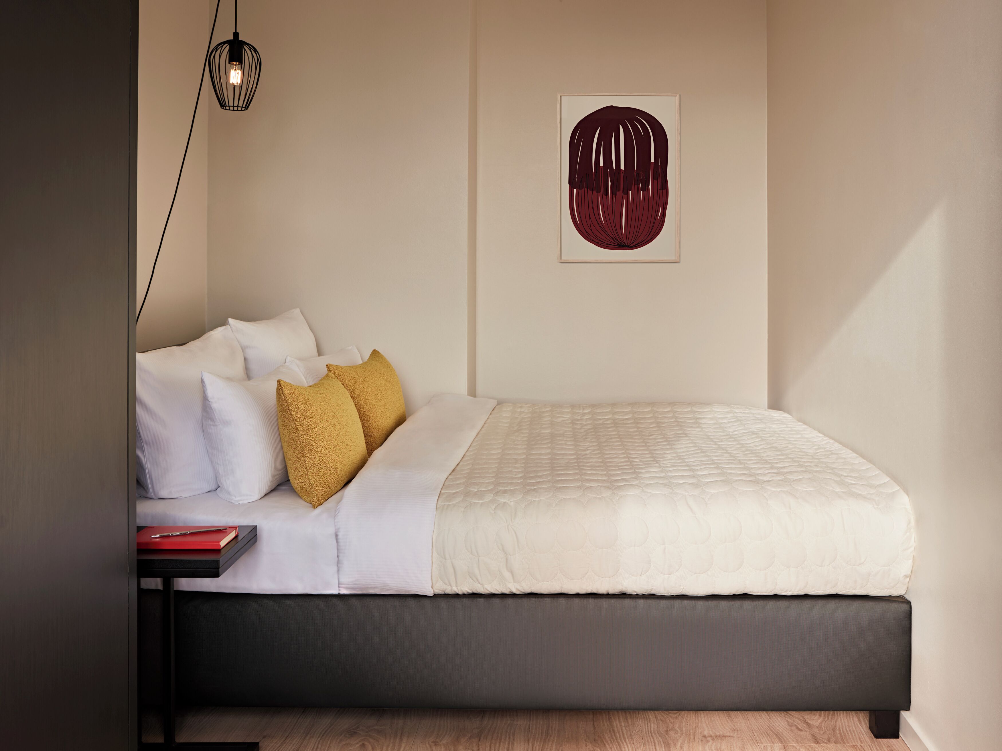 A neatly made bed with white and mustard pillows, a black headboard, and a framed artwork on the wall.