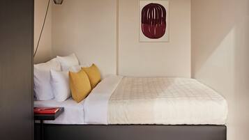 A neatly made bed with white and mustard pillows, a black headboard, and a framed artwork on the wall.