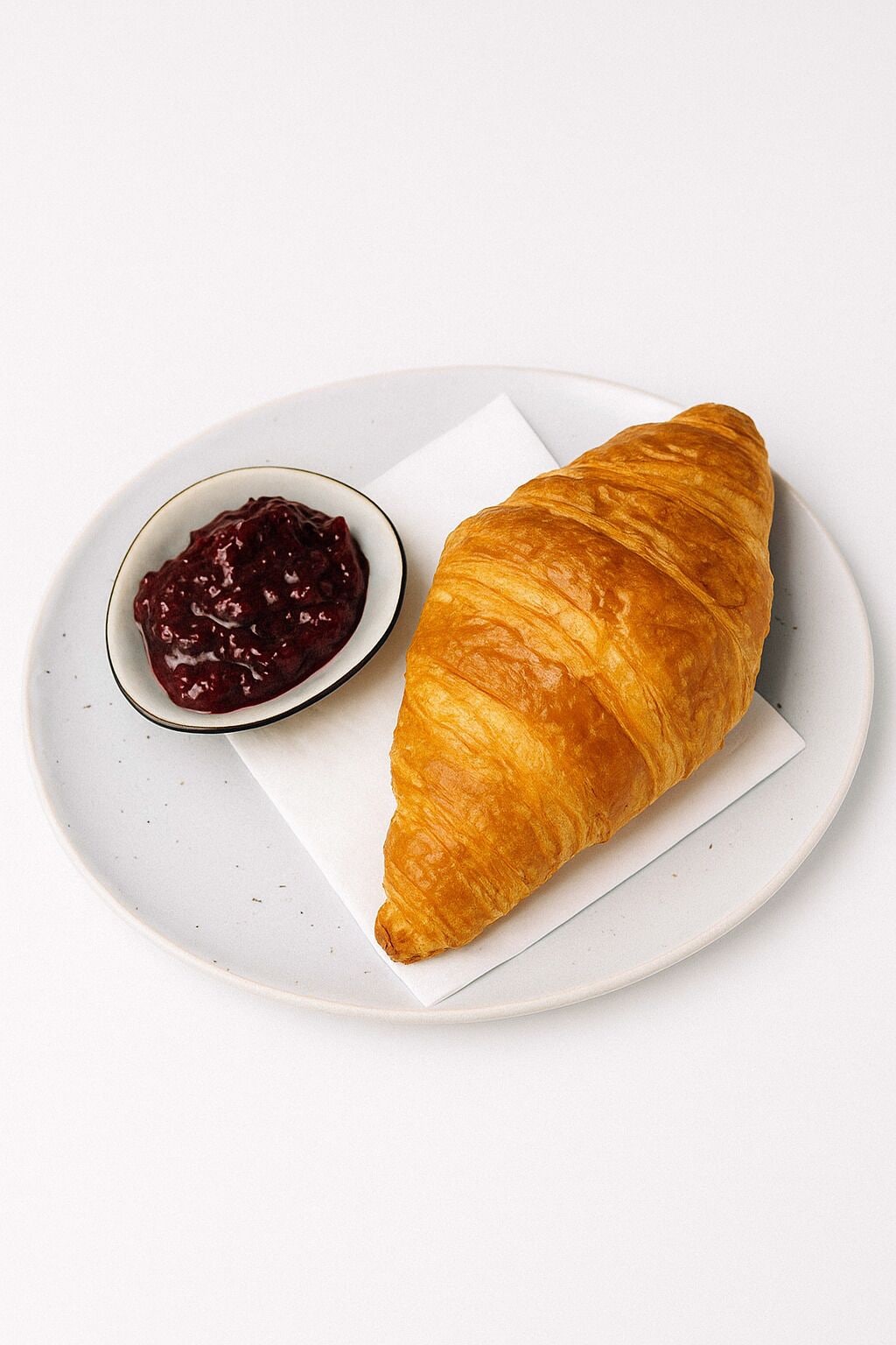 A croissant and a small bowl of jam on a white plate.