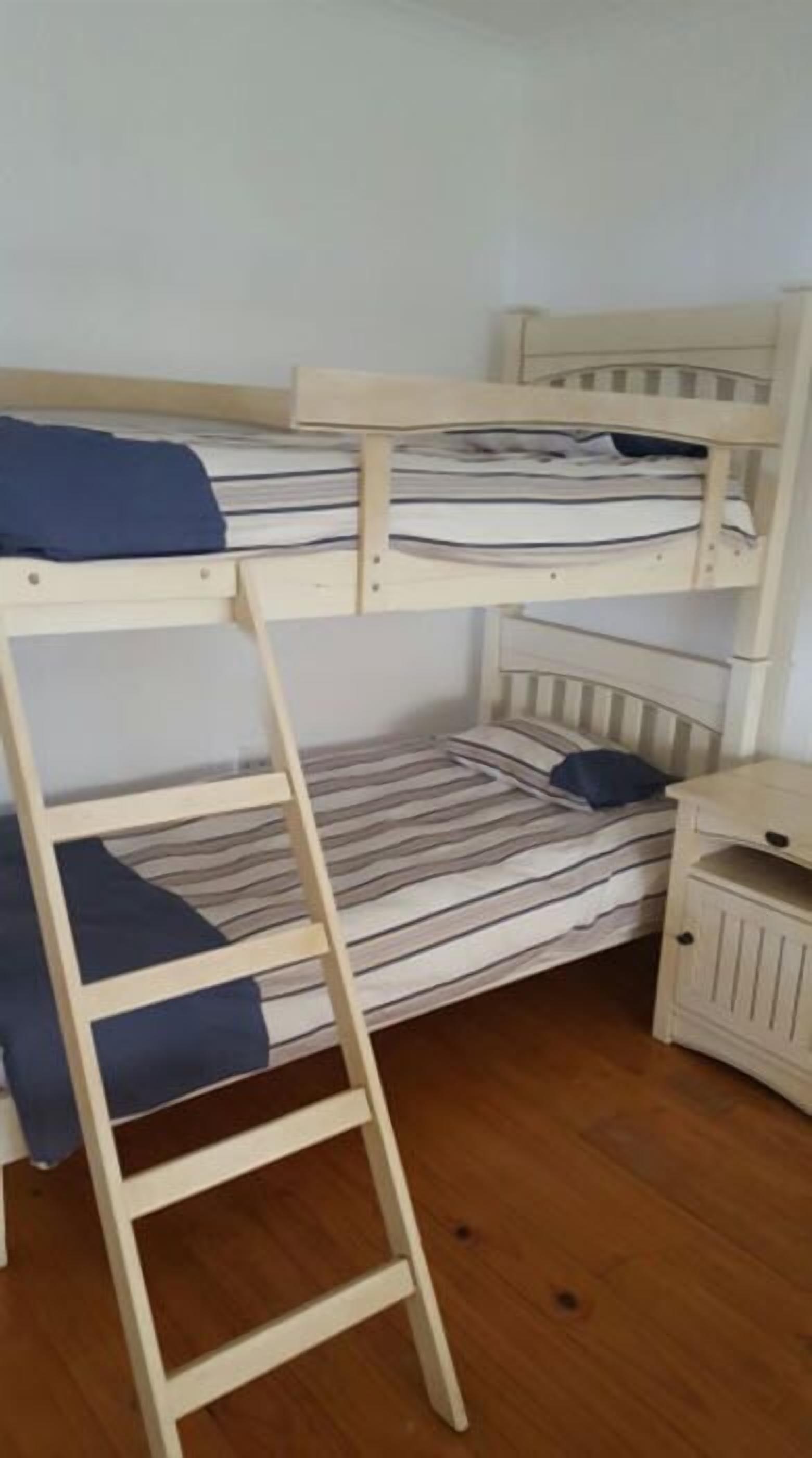 A bunk bed room with a wooden ladder, a desk, and a chair.