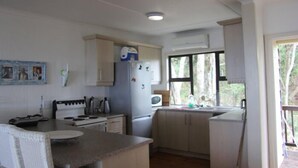 A compact kitchen with white cabinets, a stove, a microwave, and a sink. - Campismo Ninho 28 (Ponta d'Ouro)