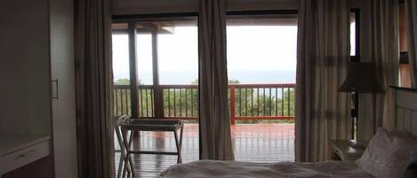 A bedroom with a large bed, a desk, and a balcony with a view.