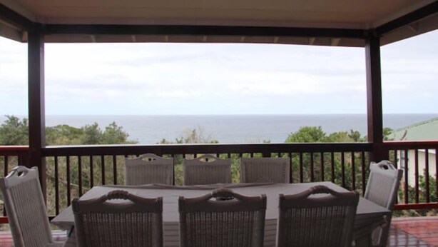 A covered outdoor seating area with a table and chairs, overlooking a scenic view of the ocean. - Campismo Ninho 28 (Ponta d'Ouro)