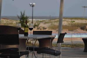 An outdoor seating area with a table and chairs, a bottle of wine, and a glass of wine. - Zalala Beach Lodge (Quelimane)