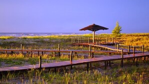 A wooden boardwalk leading to a thatched-roof structure by the beach.