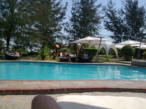 A swimming pool with lounge chairs and umbrellas, surrounded by trees and a brick border. - Zalala Beach Lodge (Quelimane)